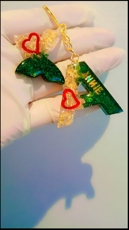Decorative earrings with green and red heart designs held by a hand against a light background.