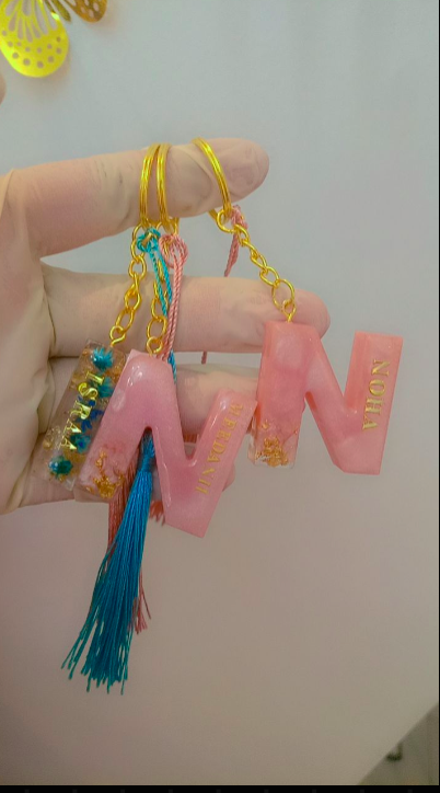 Pink letter 'W' keychain with tassel held by a hand against a white background
