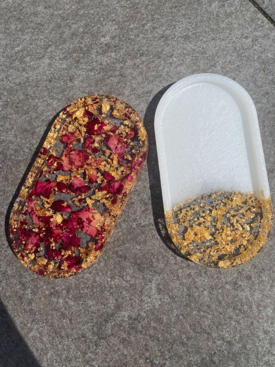 Two shoe insoles on a concrete surface, one with red and gold material, the other with white and gold.