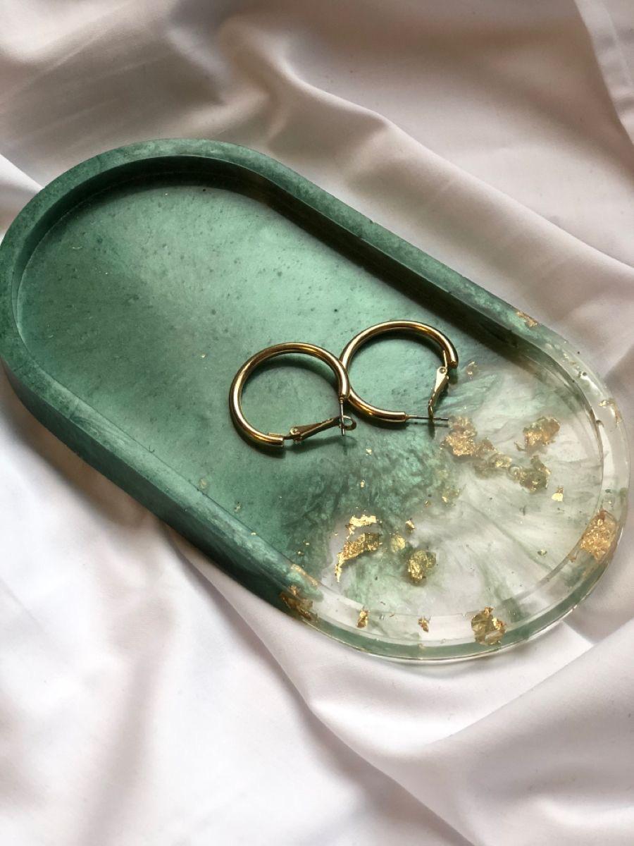 Green decorative tray with gold earrings on a white fabric background