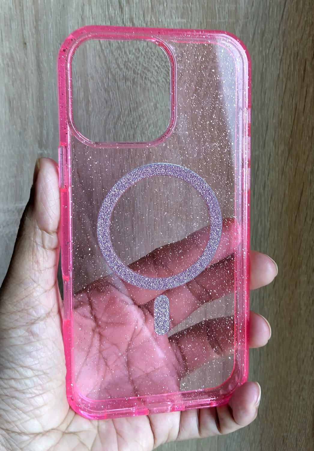 Pink glittery phone case with a ring holder held in a hand against a wooden background