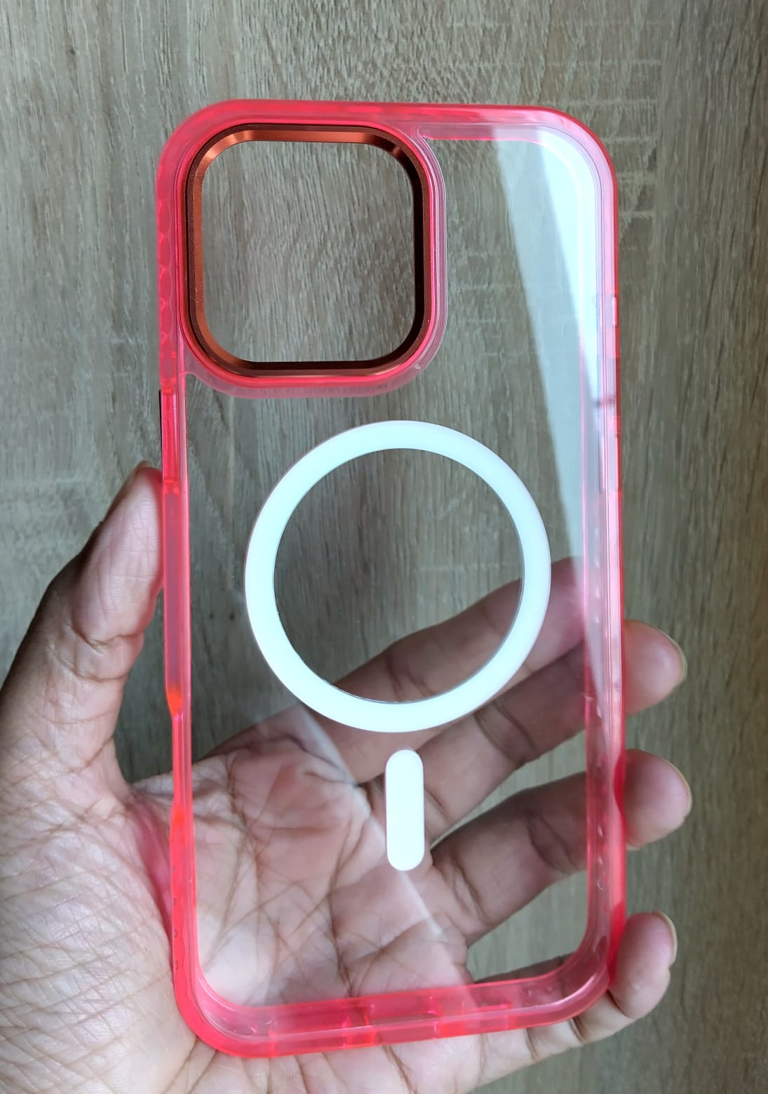 Clear phone case with red border held by a hand on a wooden surface