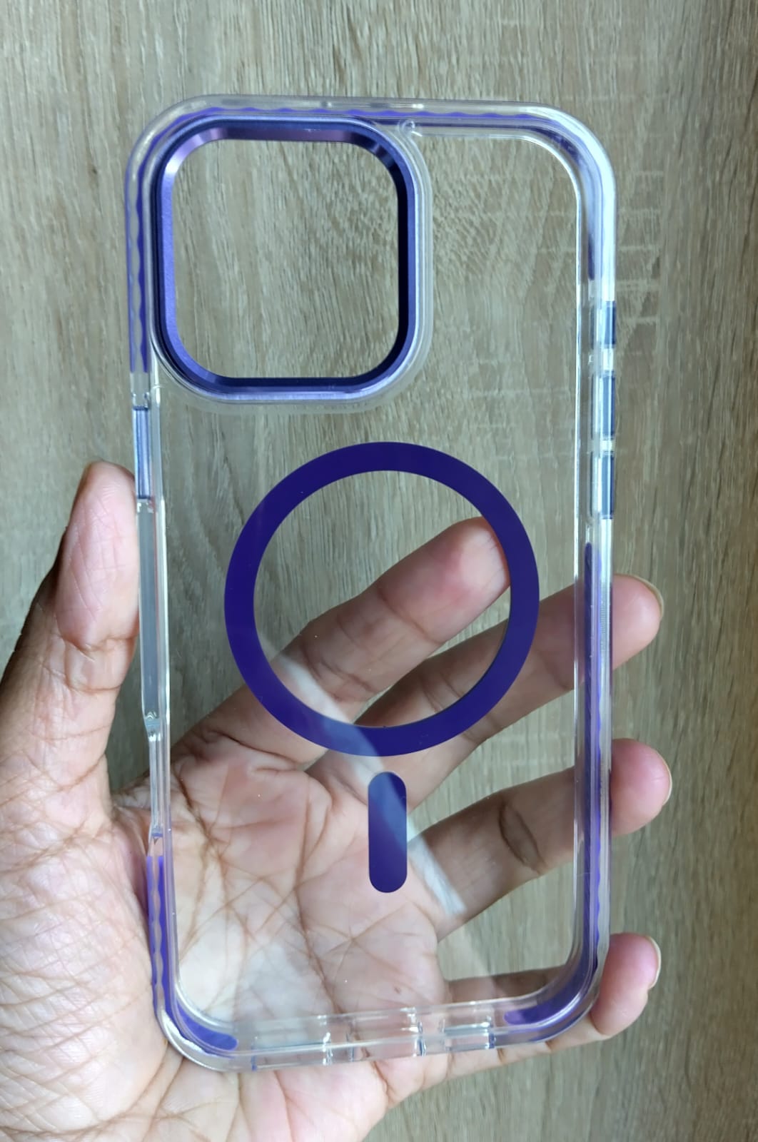 Clear phone case with purple accents held in a hand against a wooden background