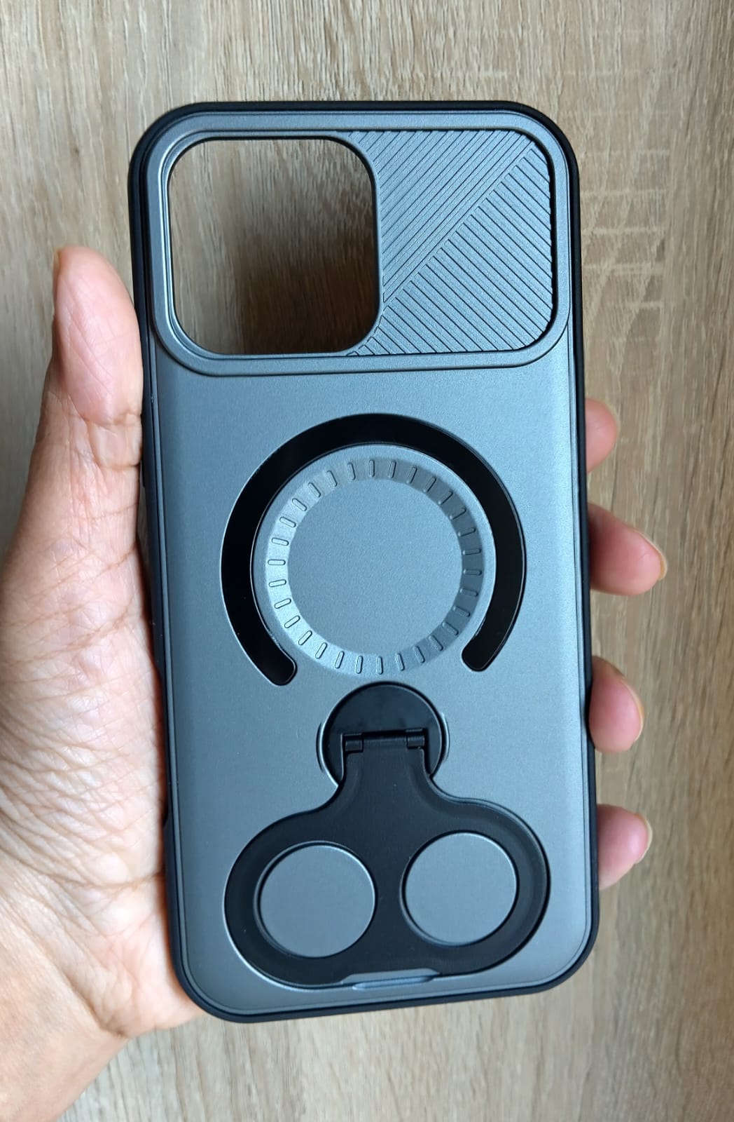 Phone case with a ring holder held by a hand on a wooden surface