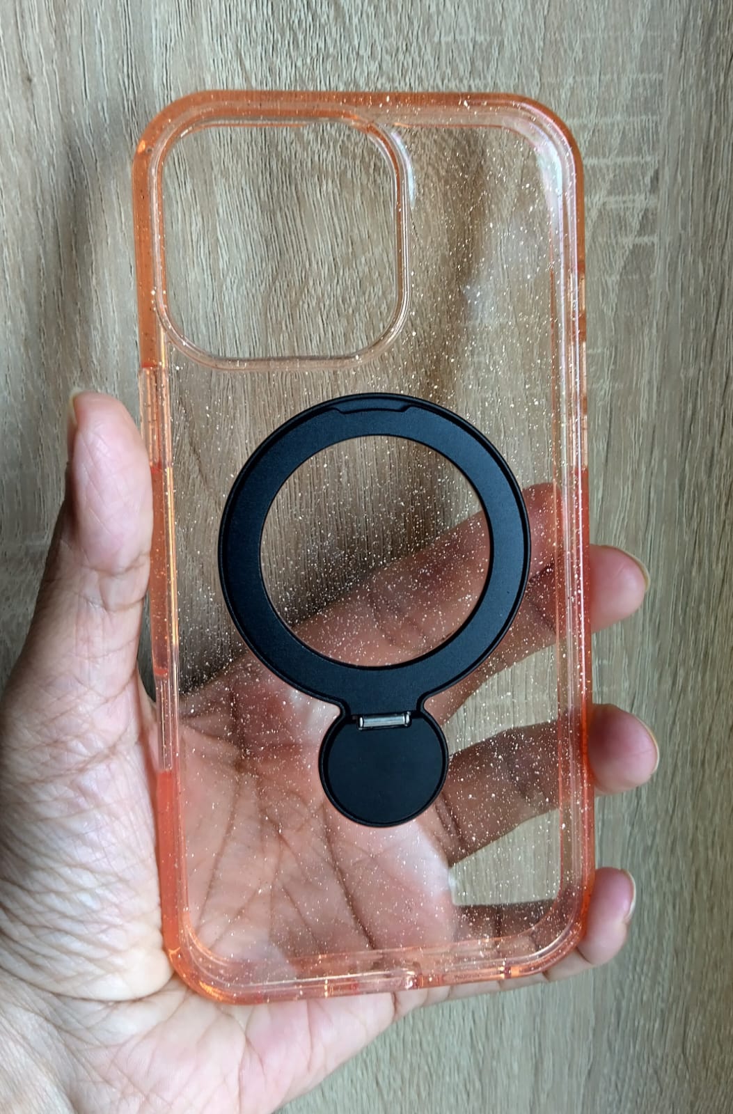 Phone case with a black ring holder held by a hand against a wooden background