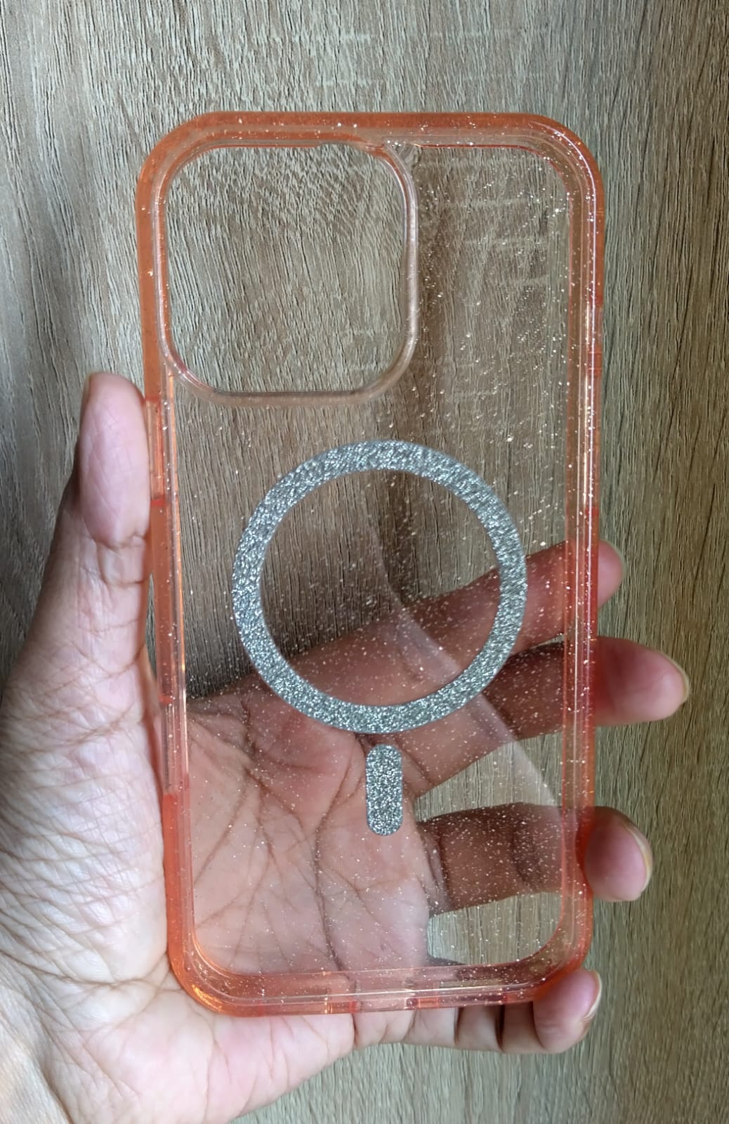 Clear phone case with a metallic ring holder held by a hand on a wooden surface