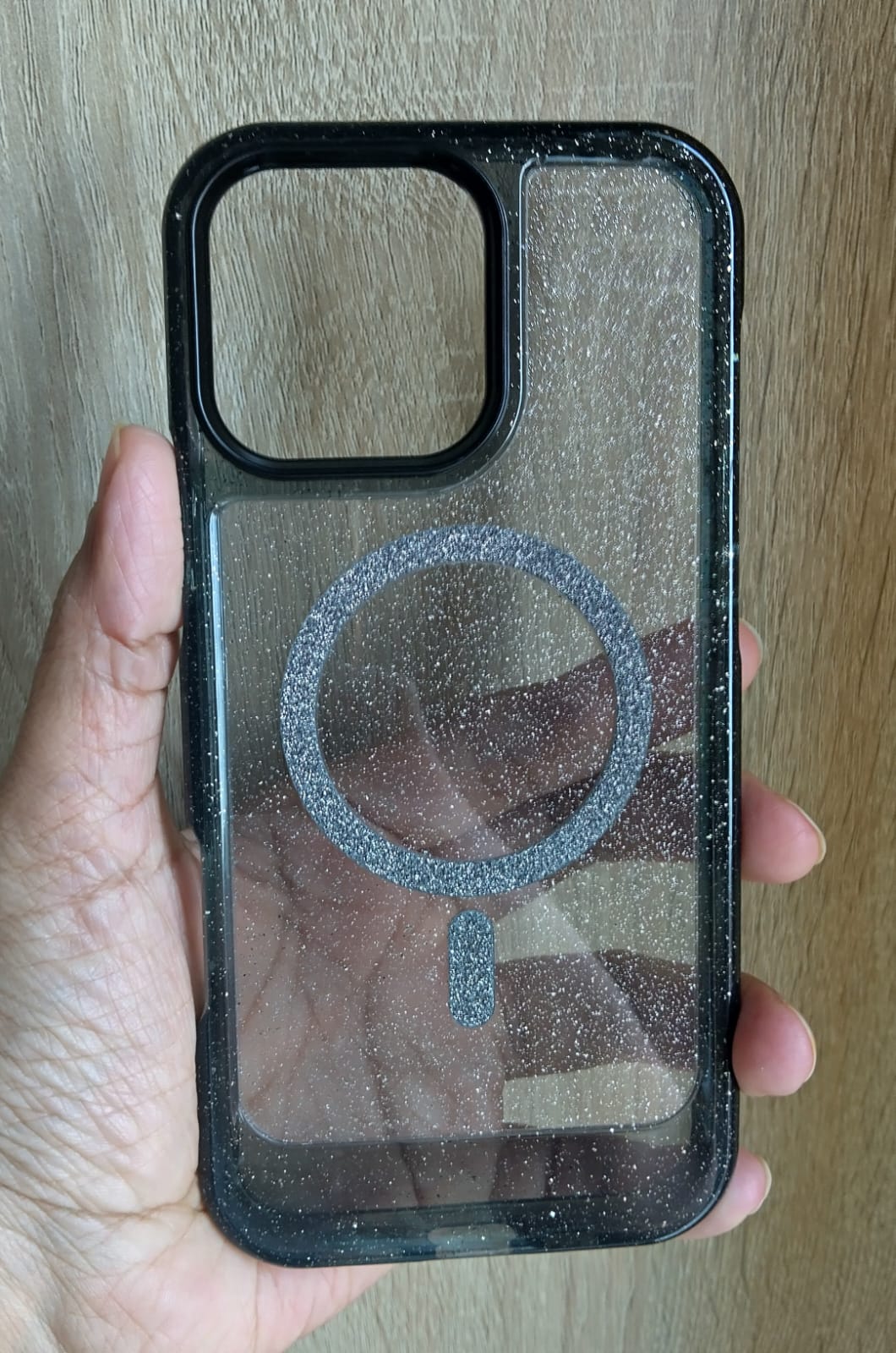 Phone case with a reflective surface held by a hand on a wooden background