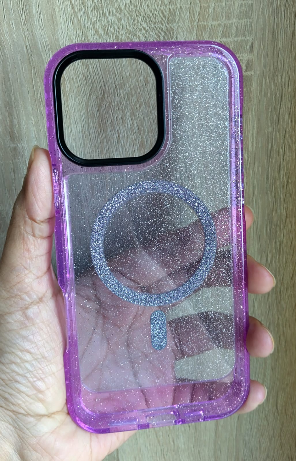 Purple glittery phone case held in a hand with a wooden background
