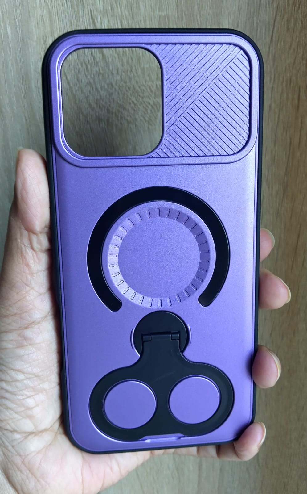 Purple phone case with a black ring holder held in a hand on a wooden surface