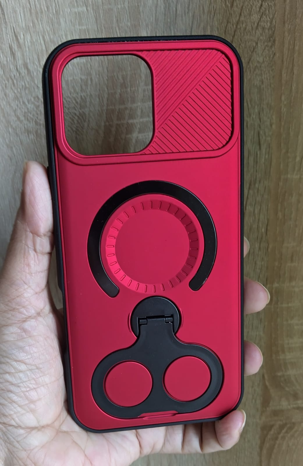 Red phone case with a black ring holder held in a hand against a wooden background
