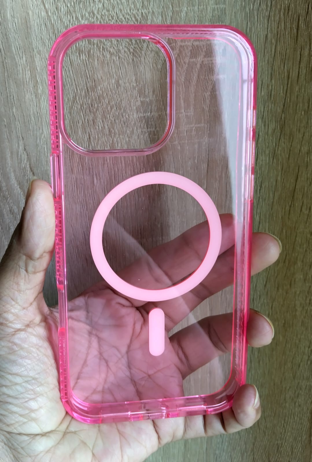 Clear phone case with pink accent held in a hand on a wooden surface