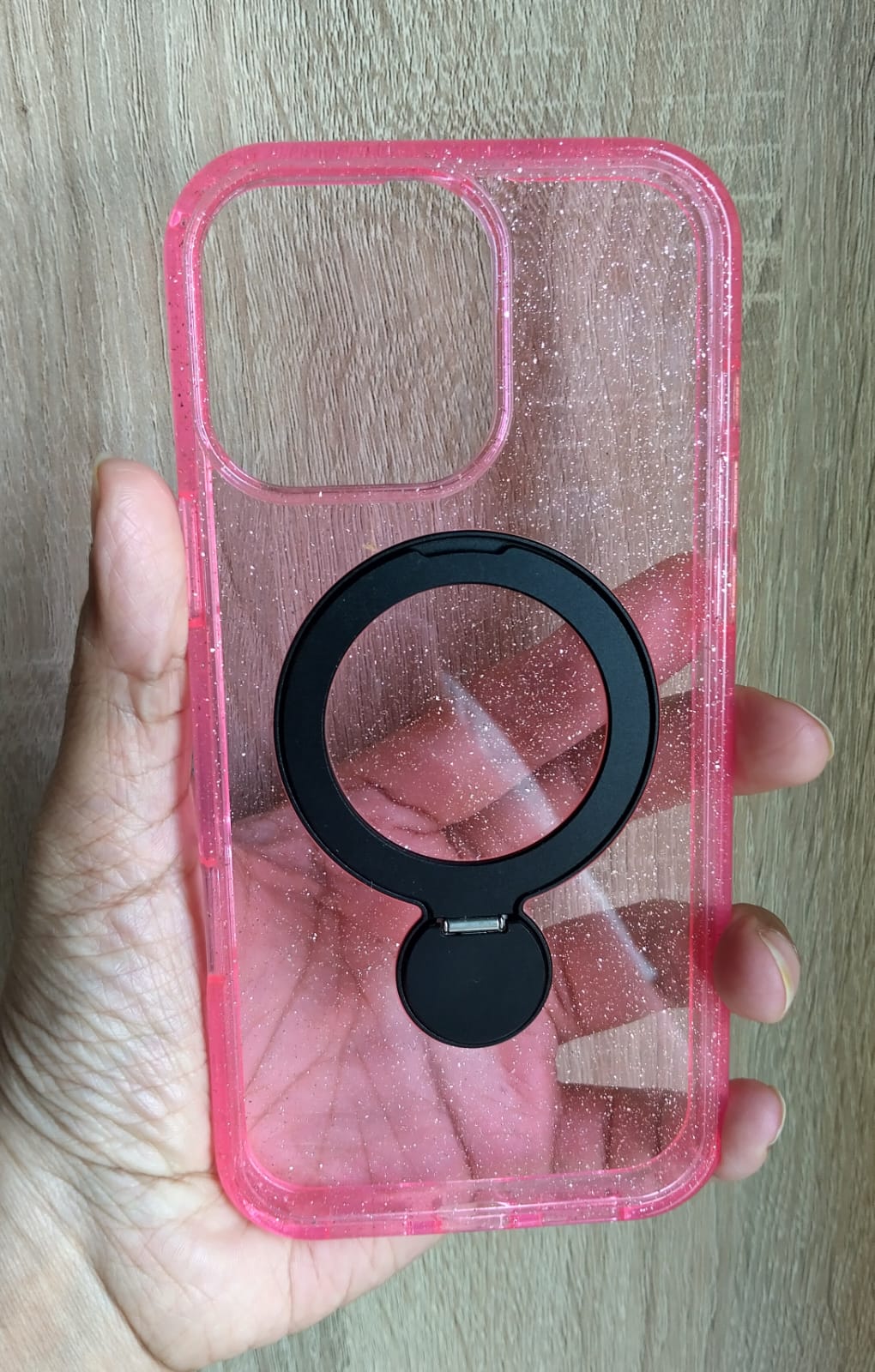 Pink phone case with a black ring holder held by a hand on a wooden surface
