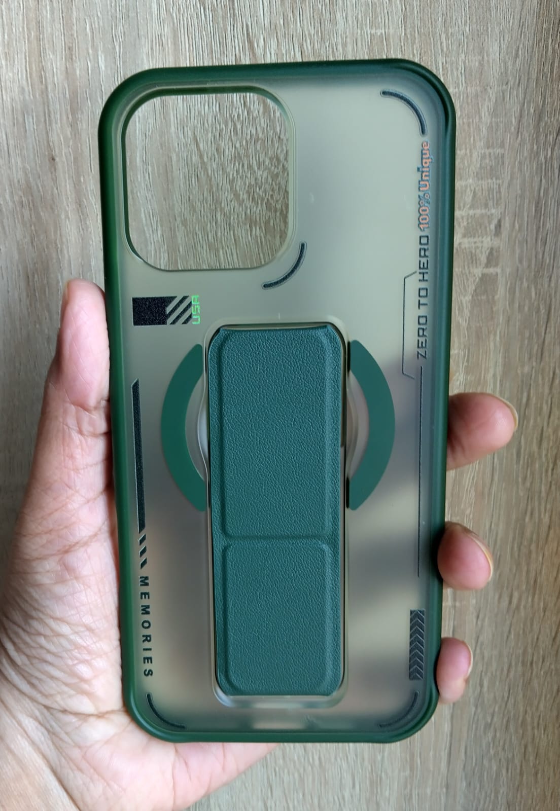 Phone case with a green grip and clear back held in a hand on a wooden surface