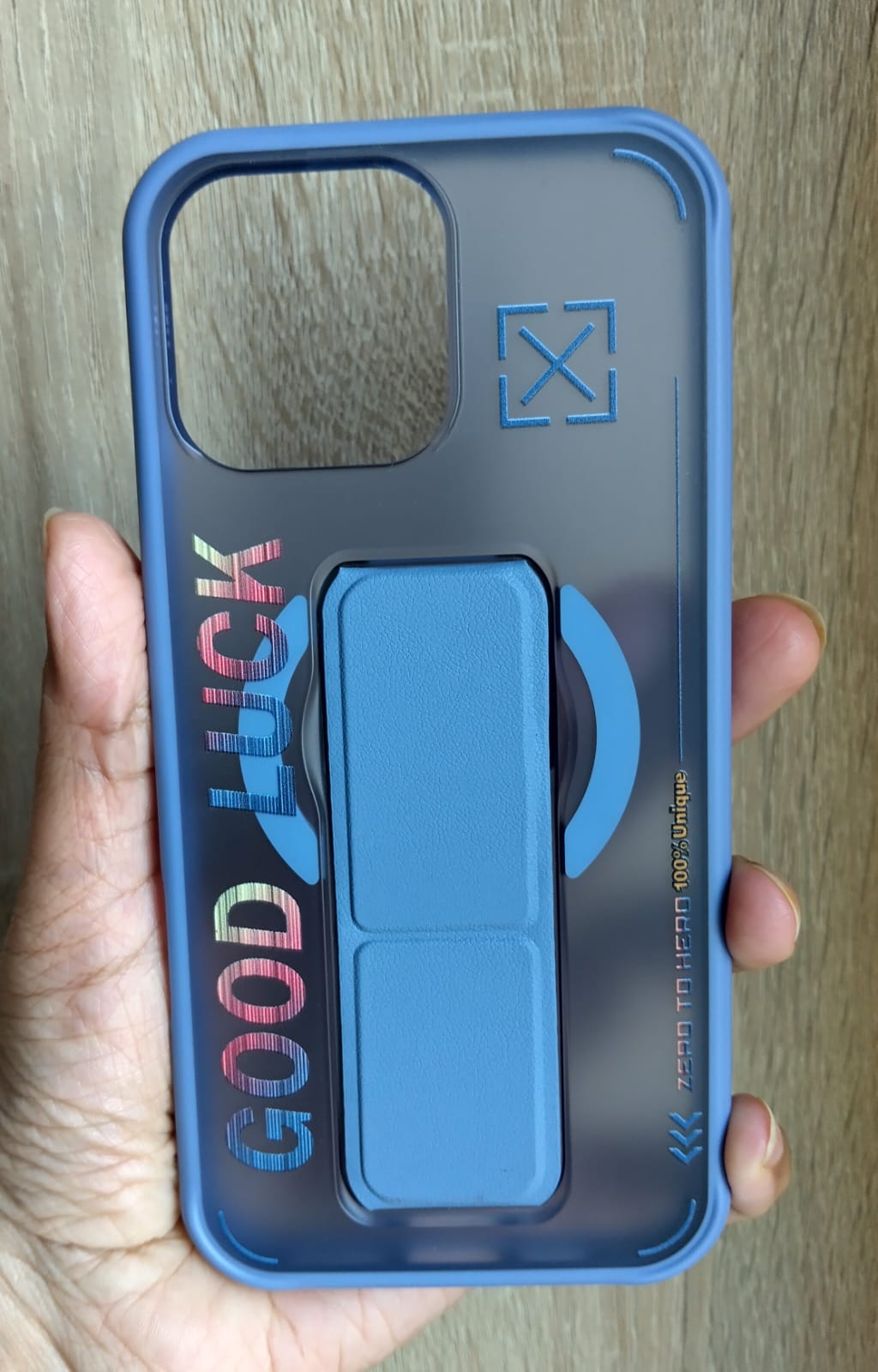 Blue phone case with 'GOOD LUCK' text held by a hand on a wooden surface