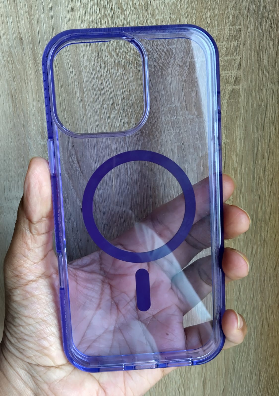 Hand holding a purple phone case with a clear design on a wooden surface