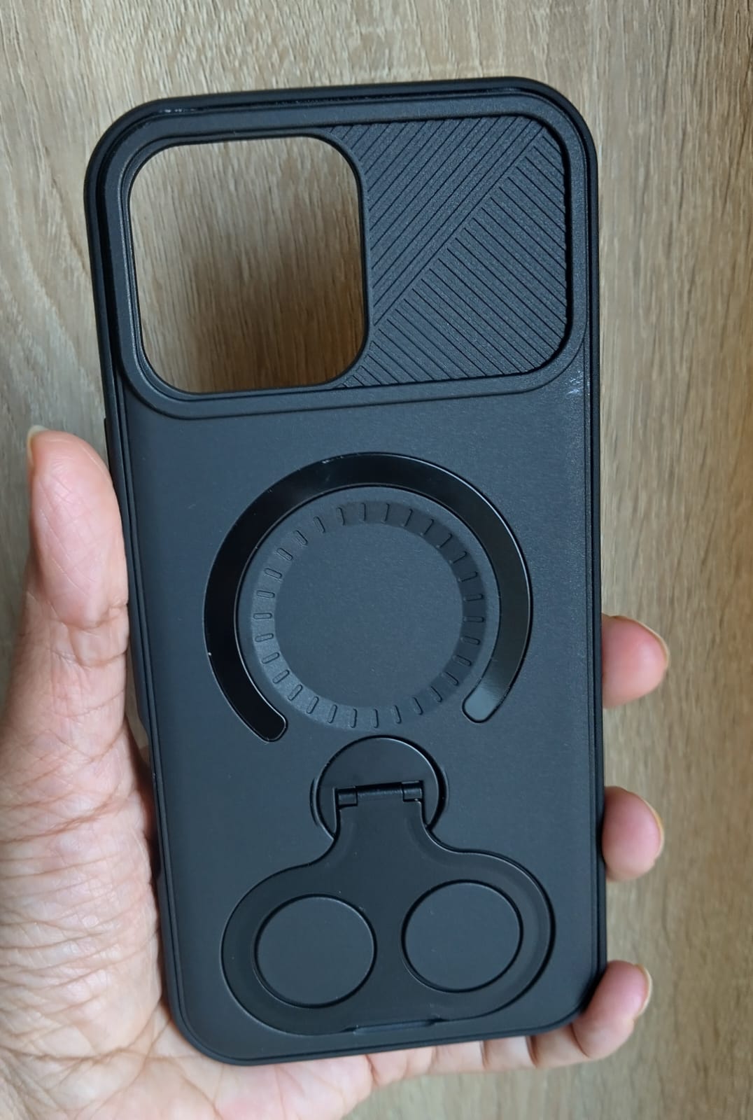 Black phone case with ring holder held by a hand on a wooden surface