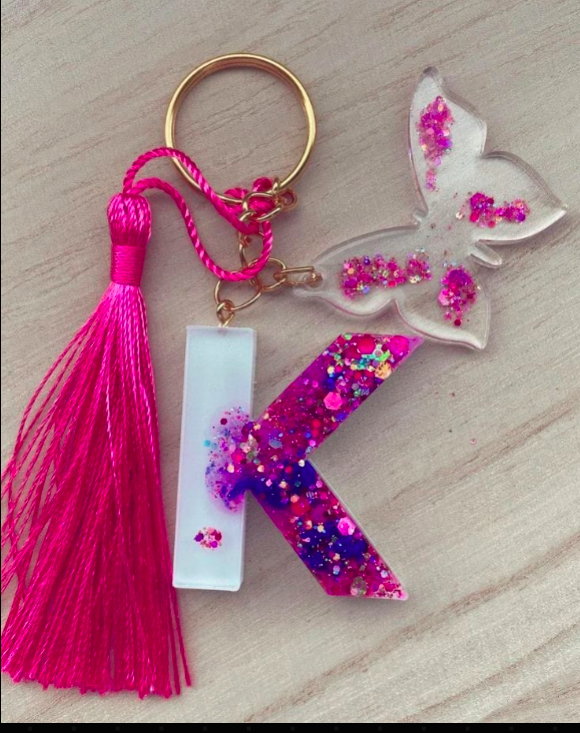 Keychain with pink tassel, letter 'K', and butterfly design on a wooden surface