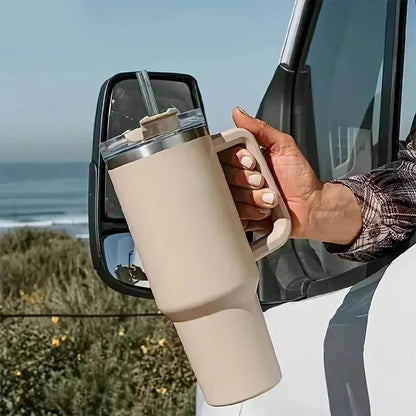 Person holding a beige travel mug with a straw, parked by a car window with a scenic background.