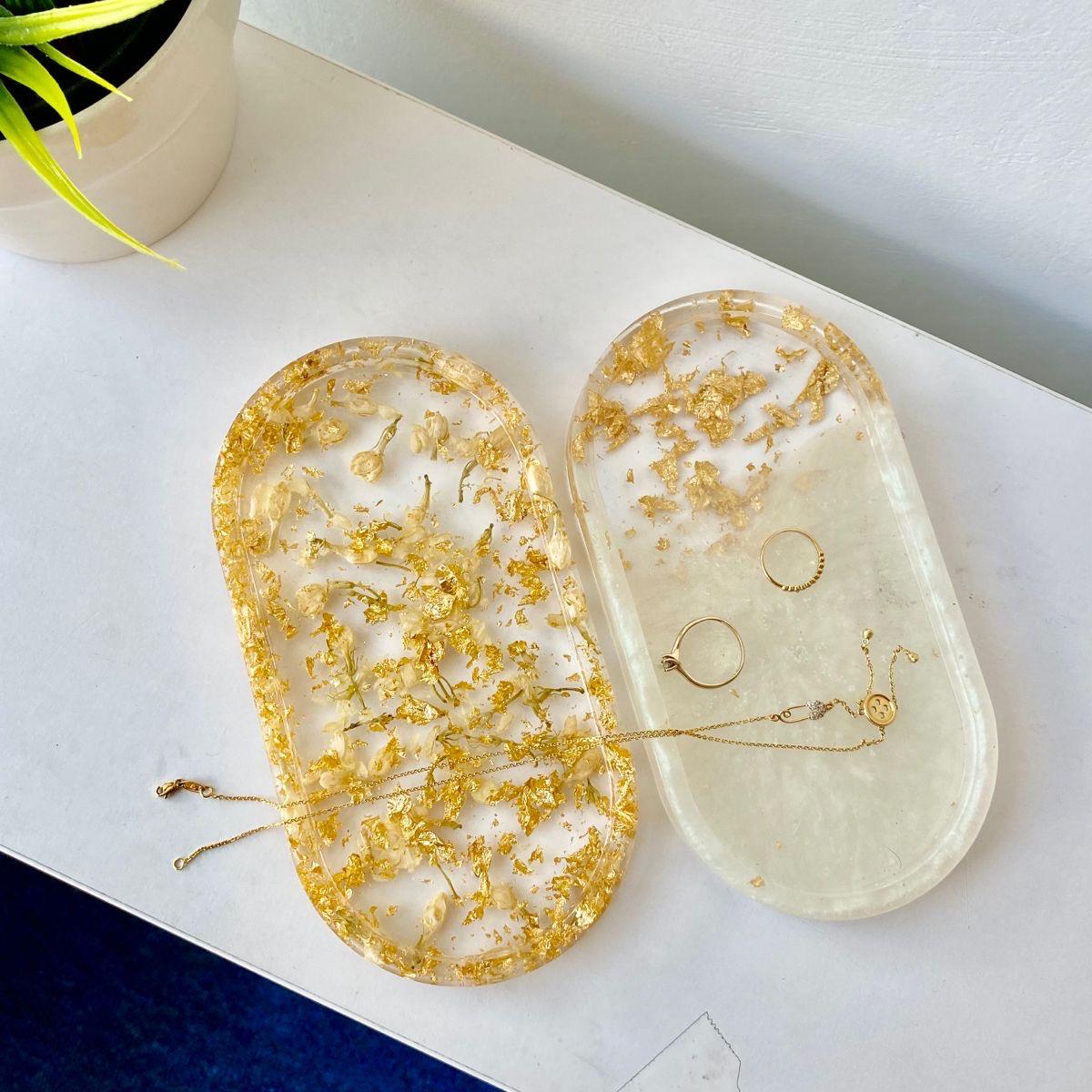 Two oval resin jewelry displays with gold leaf on a white surface.