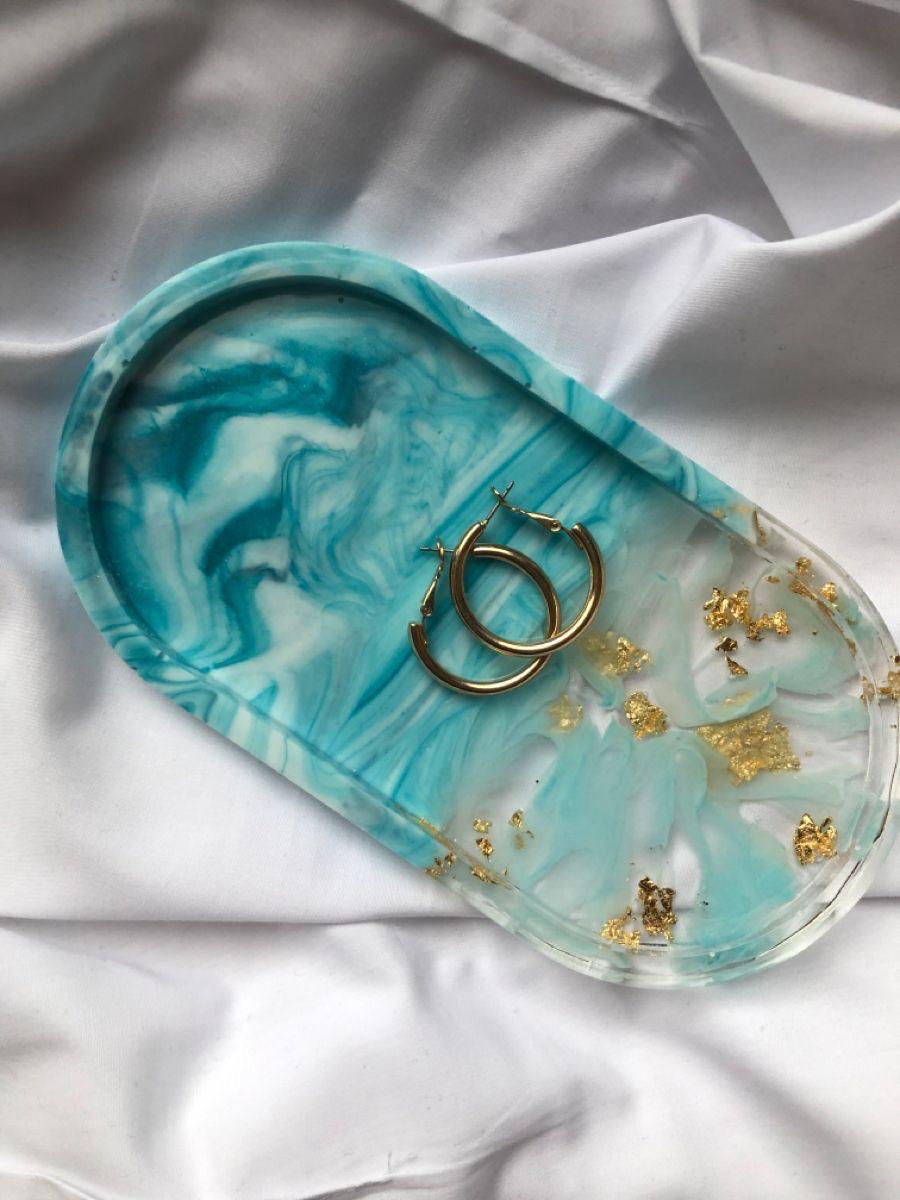 Turquoise marbled jewelry tray with gold accents on a white fabric background