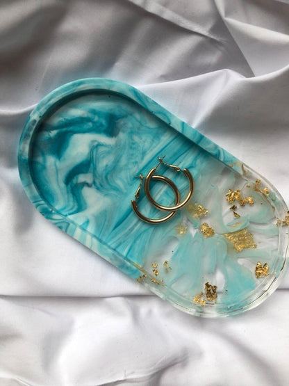 Turquoise marbled jewelry tray with gold accents on a white fabric background